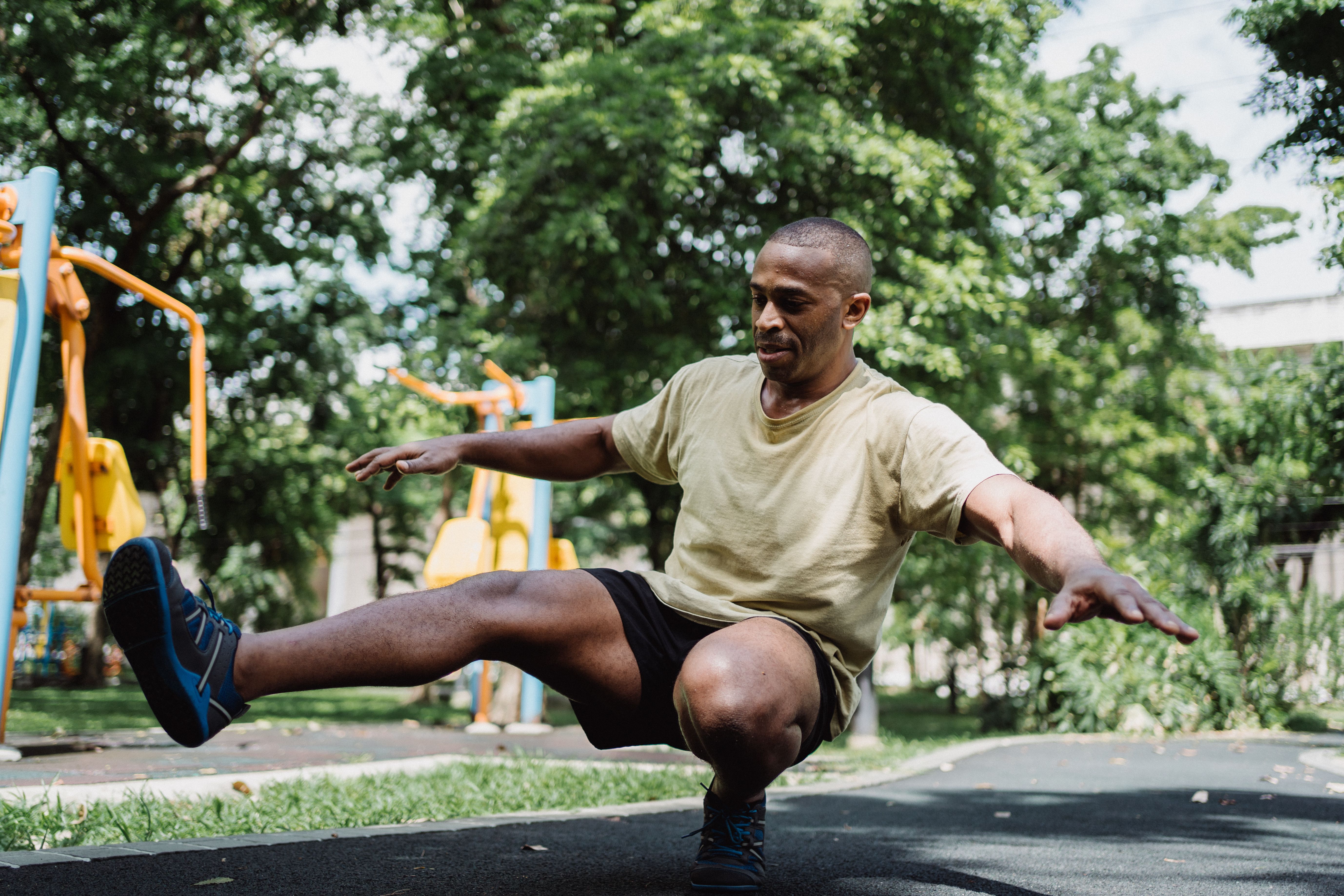 An adult man controlling a single-leg squat outdoors with his arms extended and the other leg reaching forward.
