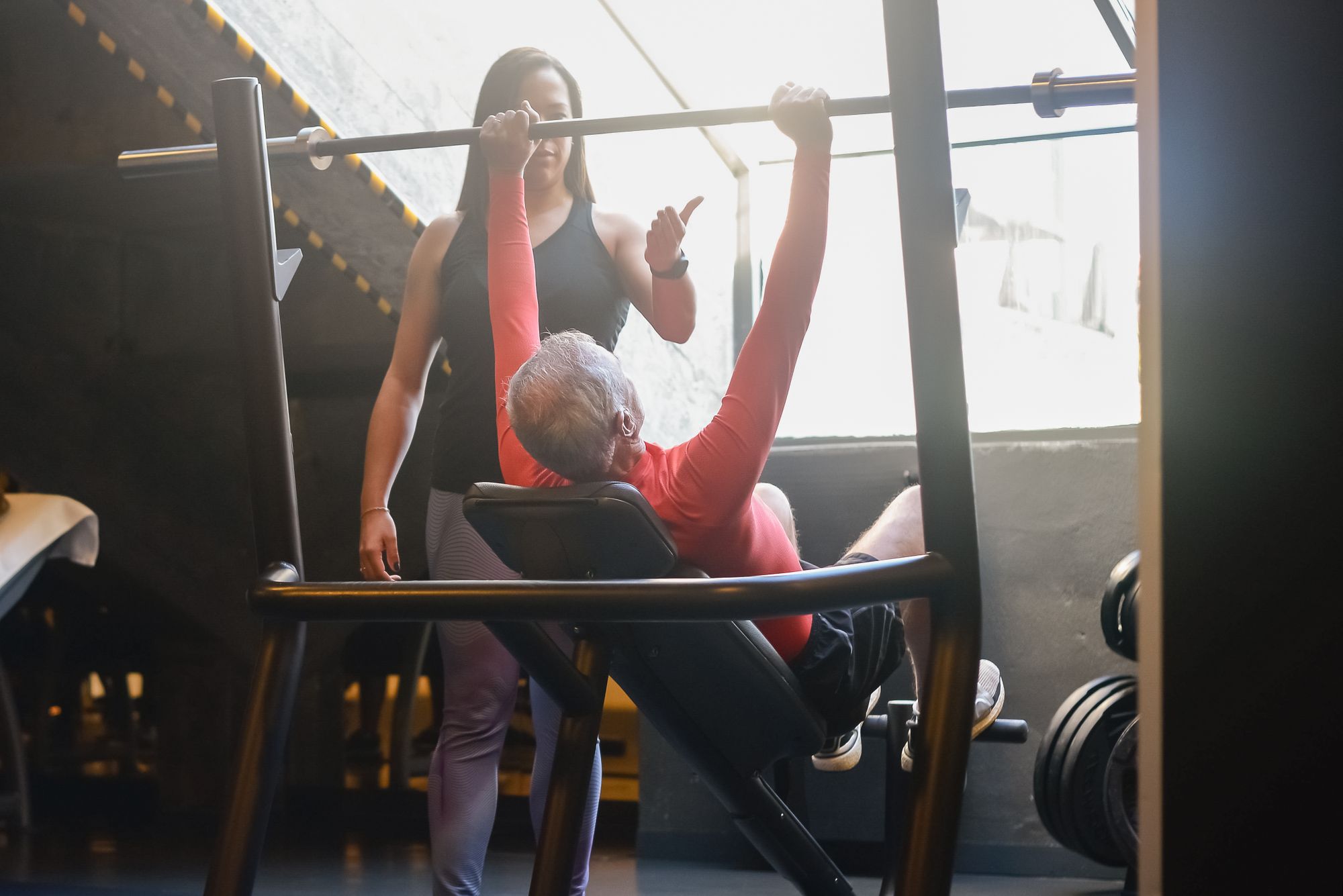 Adult performing an incline barbell press with a trainer supervising in a gym.