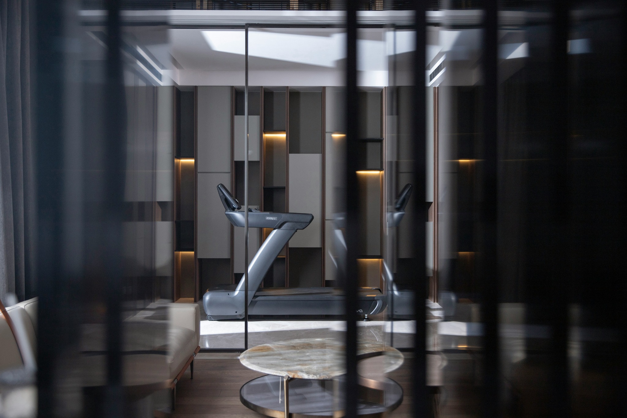 A treadmill integrated into a refined interior with timber flooring, glass partitions and warm architectural lighting