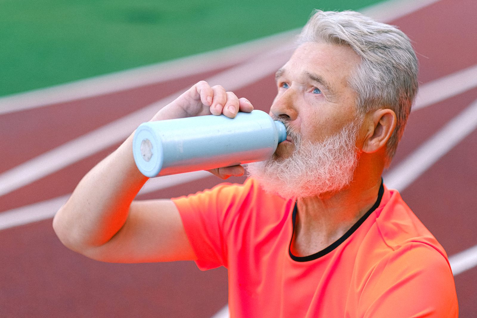 An active adult drinks from a reusable bottle beside an outdoor running track.